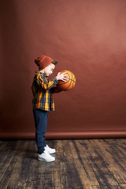 Stylish boy playing basketball. Studio shot, brown background  - Фото, зображення