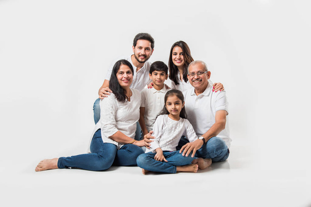 Famille indienne assise sur fond blanc. couple senior et jeune avec des enfants portant un haut blanc et un jean bleu. focus sélectif - Photo, image