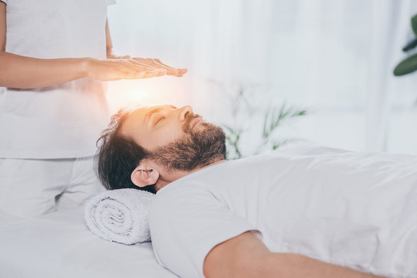 cropped shot of calm bearded man with closed eyes receiving reiki treatment above head   - Photo, Image