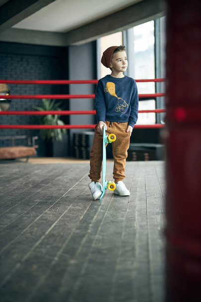 Little stylish boy skateboarding on boxer ring - Foto, imagen