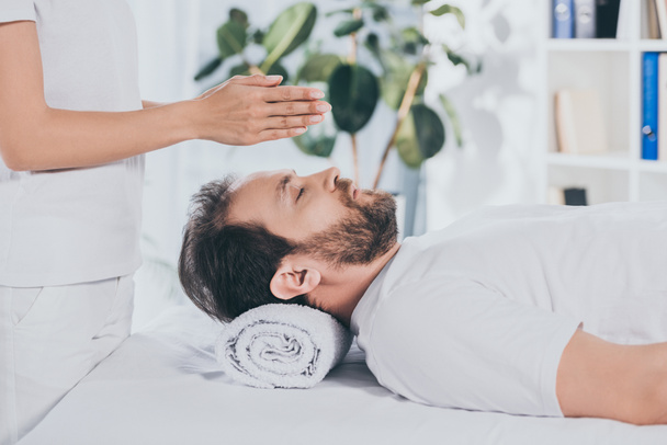 side view of bearded man with closed eyes receiving reiki treatment above head - Photo, Image