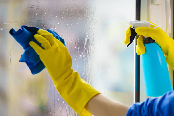 Ženská ruka ve žlutých rukavicích čistící okenní tabule s hadrem a čisticím prostředkem. Koncept čištění - Fotografie, Obrázek