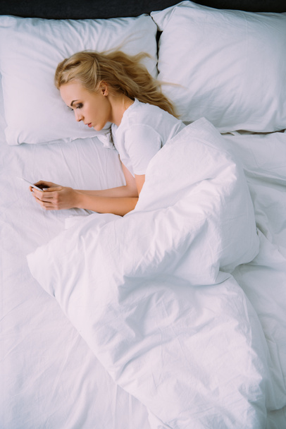 sad lonely woman lying in bed and using smartphone - Photo, Image