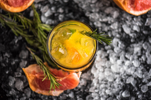 Cocktail in glass with grapefruit and rosemary on dark background with ice - Фото, зображення
