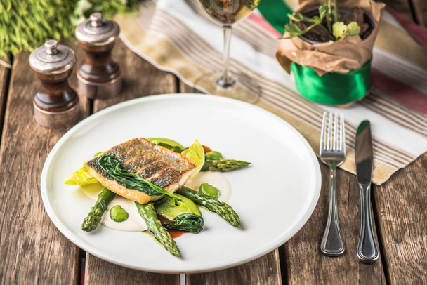 Roasted fish fillet with green asparagus served on white plate on wooden table - Photo, image