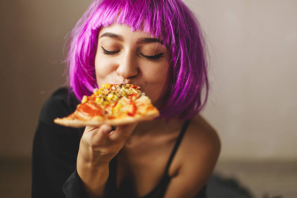 Смешной розовый парик девушка в черном нижнем белье и рубашка ест пиццу дома. Девушка наслаждается вкусной пиццей
 - Фото, изображение