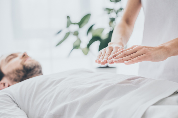 cropped shot of bearded man lying and receiving reiki treatment on stomach - Фото, изображение