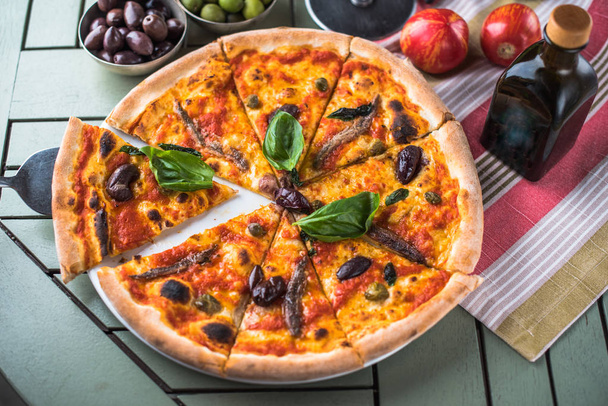 freshly baked pizza with anchovies on table with ingredients - Фото, зображення