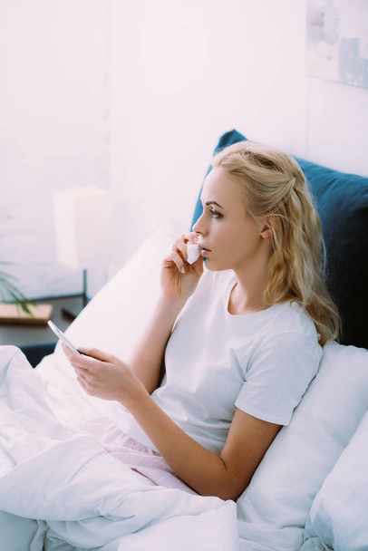 mulher triste limpando lágrimas e usando smartphone na cama em casa
 - Foto, Imagem