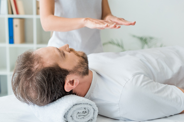 cropped shot of bearded man lying on massage table and receiving reiki treatment  - Photo, Image