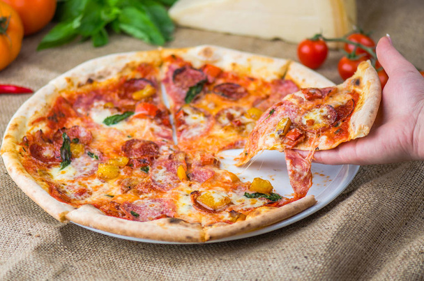 menschliche Hand hält ein Stück italienische Pizza mit Salami und Tomatensauce über einem Sacktuch - Foto, Bild