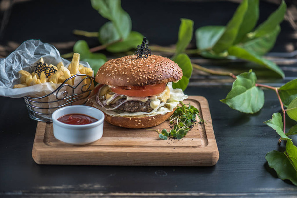 Burger with potato fries served on wooden board on dark background with leaves - Fotoğraf, Görsel