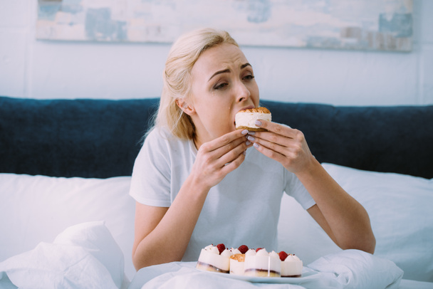 przygnębiony Kobieta w piżamie jeść słodkie ciasto w łóżku sam - Zdjęcie, obraz