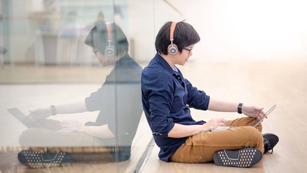 Aziatische zakenman muziek beluisteren door de koptelefoon terwijl u werkt met laptopcomputer in coworking space. Freelance of Digitaal Nomade levensstijl. Online winkelen of E-commerce social media op internet - Foto, afbeelding