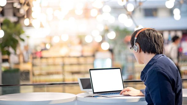 asiatischer Geschäftsmann, der Musik über Kopfhörer hört, während er mit Laptop im Coworking Space arbeitet. freiberuflicher oder digitaler Nomaden-Lebensstil. Online-Shopping oder E-Commerce Social Media im Internet - Foto, Bild