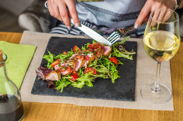 hands of woman eating salad served on slate on table in cafe - Fotoğraf, Görsel