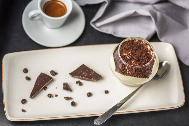 close-up view of delicious tiramisu dessert in glass, spoon, chocolate, coffee beans and cup of coffee on table - Zdjęcie, obraz
