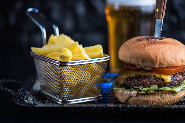 Beef burger served on platter with fried potato wedges on dark background - Фото, изображение