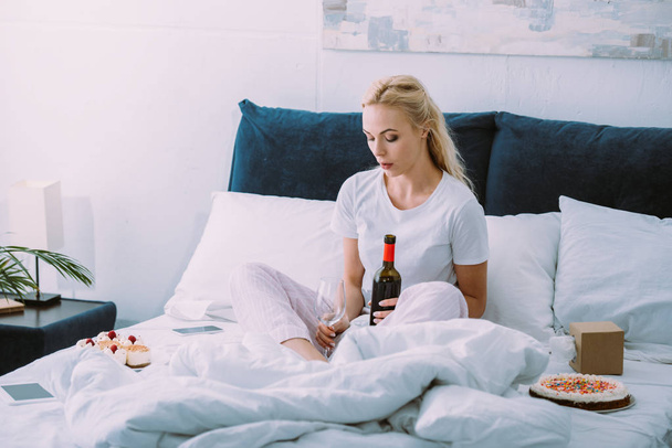 Traurige Frau mit Glas und Flasche Wein feiert Geburtstag allein im Bett - Foto, Bild