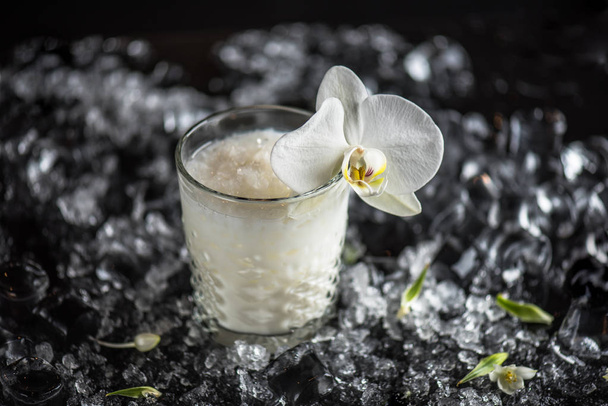 Cocktail in glass decorated with orchid flowers on dark background with ice - Foto, immagini