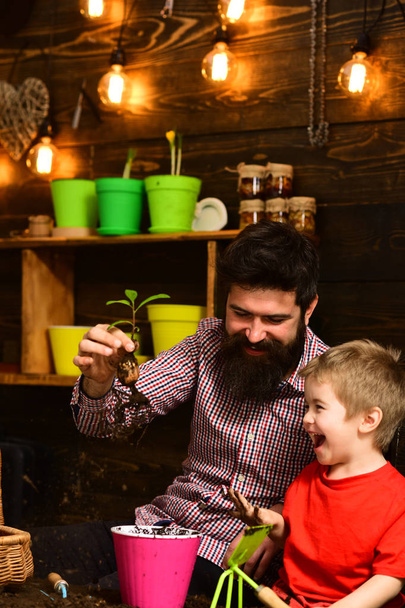 happy gardeners with spring flowers. Flower care watering. Soil fertilizers. Family day. Greenhouse. bearded man and little boy child love nature. Father and son - Foto, afbeelding