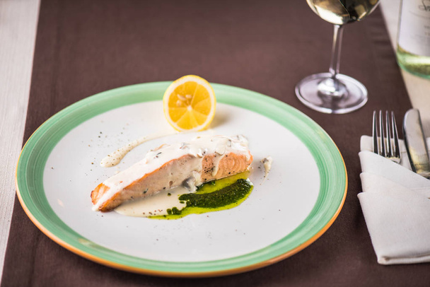 Kawałek łososia na parze z sosem na talerzu z kieliszek białego wina - Zdjęcie, obraz