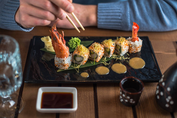 close-up of person eating sushi roll served on slate with wasabi and ginger - Foto, Imagem
