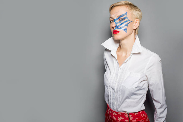 young woman in white shirt and blue stripes on face, red lipstick isolated over grey - Foto, afbeelding