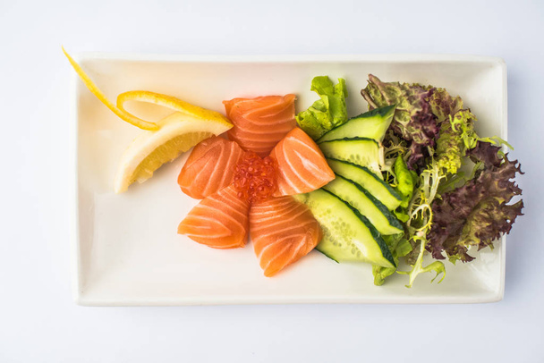 Fresh salmon sashimi with red caviar and vegetables served on platter on white background - Photo, image