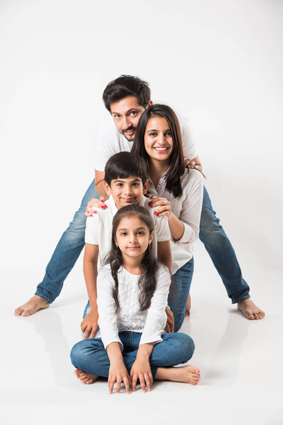heureuse famille indienne de 4 debout isolé sur fond blanc. Jeune couple avec des enfants portant un haut blanc et un jean bleu. focus sélectif - Photo, image