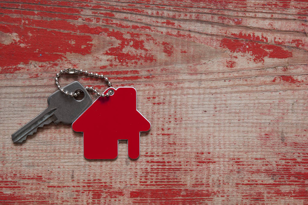 Fermer les clés de la maison sur un porte-clés en forme de maison sur fond en bois. Concept pour l'immobilier, le déménagement ou la location de biens sur bois rouge
 - Photo, image