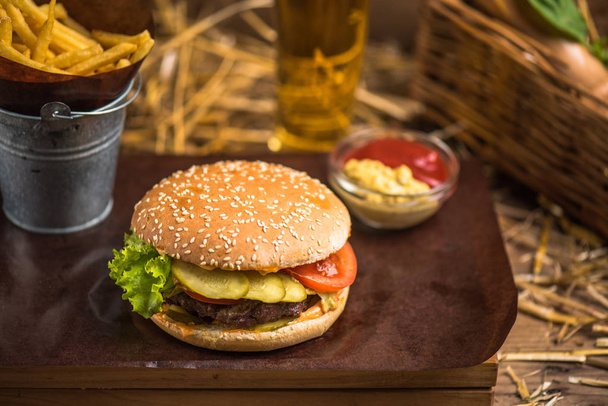 Tasty burger with french fries on wooden board - Фото, изображение