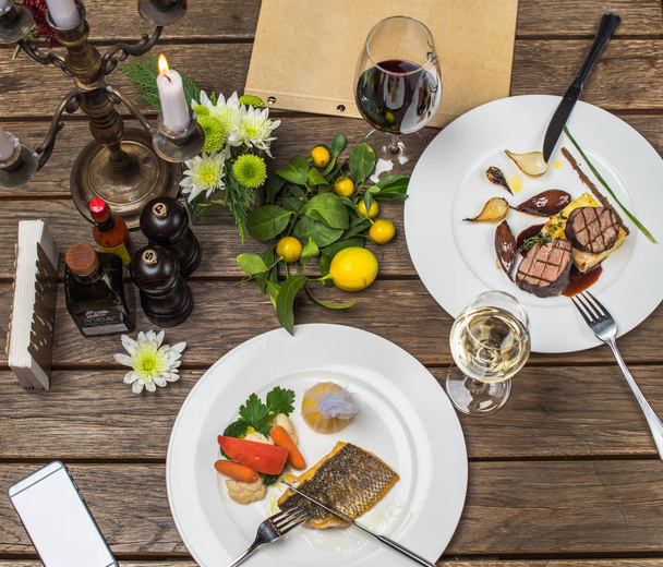 de instelling van de houten tafel met vlees- en visgerechten geserveerd op witte platen - Foto, afbeelding