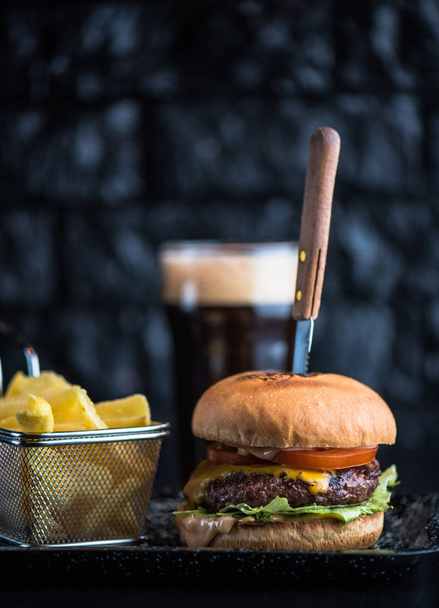 Beef burger served on platter with fried potato wedges on dark background - Foto, afbeelding