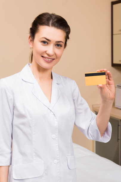 esteticista segurando cartão de crédito e sorrindo no salão de beleza
 - Foto, Imagem