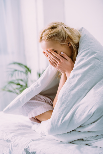 woman in blanket covering face with hands and crying in bed at home  - Foto, afbeelding