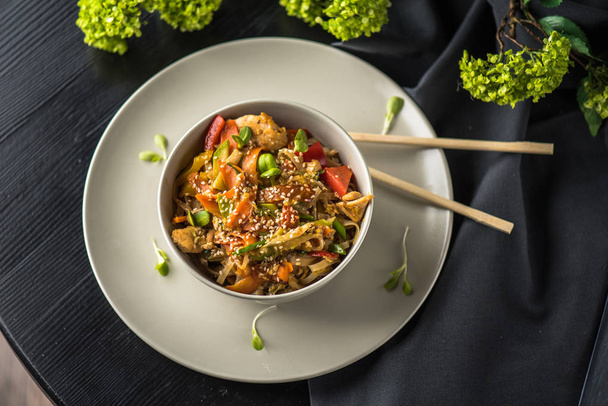 Bowl of asian noodles on plate with chopsticks on black fabric - Fotó, kép
