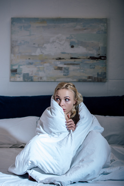 frightened woman covered in blanket looking away in bedroom - Foto, Imagem