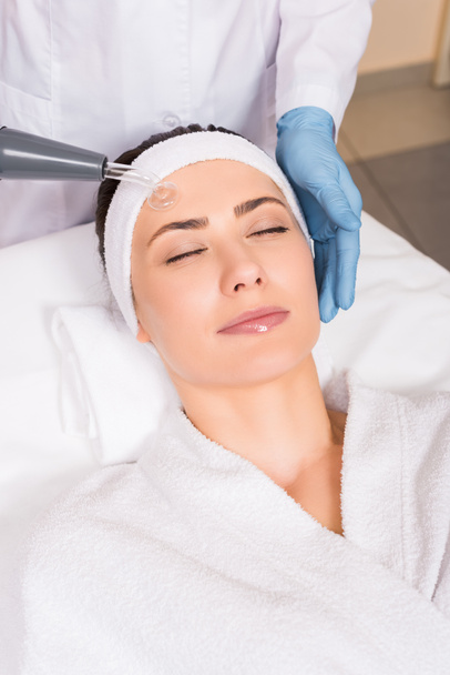beautician doing darsonvalization to woman on face at beauty salon - Photo, Image