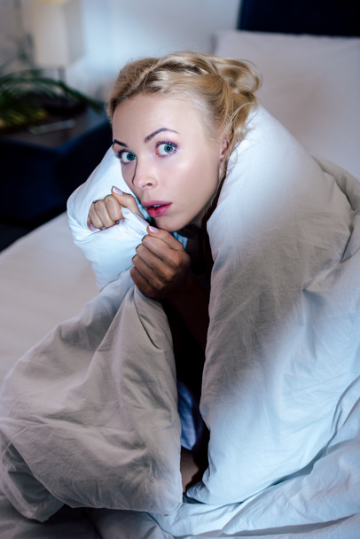 frightened woman covered in white blanket looking at camera in bed  - Photo, image