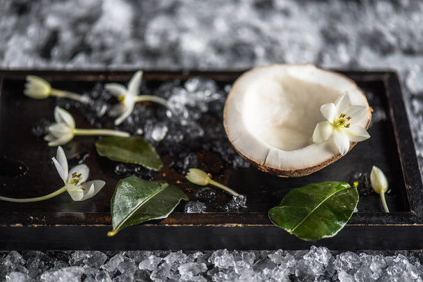 La moitié de noix de coco fraîche sur un plateau avec glace, feuilles et fleurs
 - Photo, image