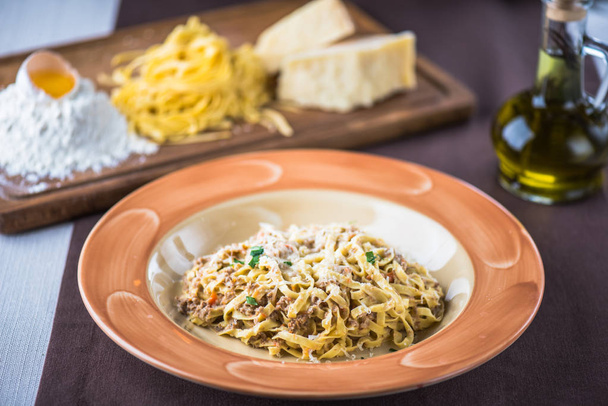 Plaat van zelfgemaakte pasta met vlees en kaas op tafel met ingrediënten - Foto, afbeelding