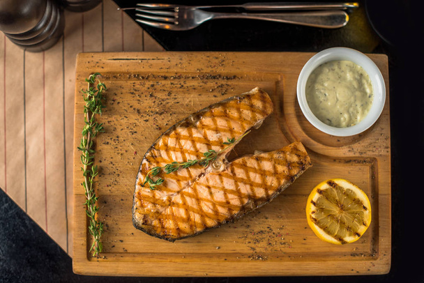 Grilled piece of salmon on wooden board with dip and lemon - Photo, image