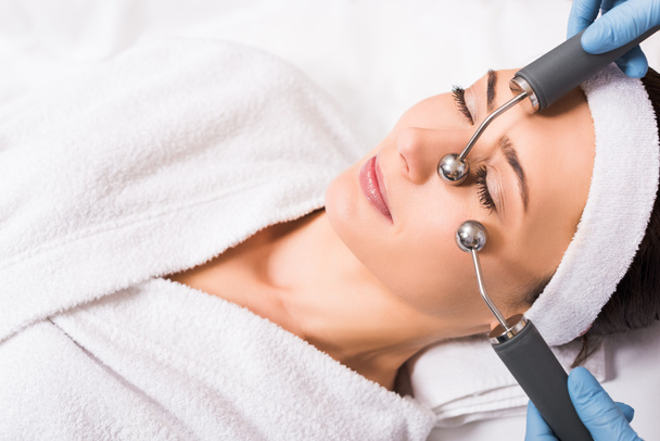 жінка лежить косметолог робить масаж обличчя з обладнанням в салоні краси
 - Фото, зображення