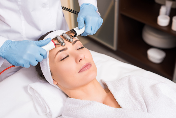 cosmetologist doing face massage by equipment to woman at beauty salon - Valokuva, kuva