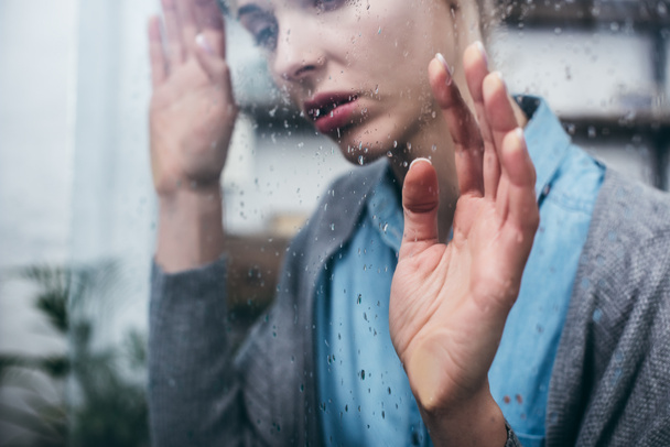 Kırpılan üzgün yetişkin kadın yağmur damlaları ile ev dokunaklı pencere görünümünü - Fotoğraf, Görsel