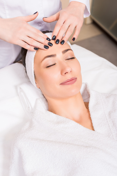 esteticista dando massagem facial manual para a mulher deitada no salão de beleza
 - Foto, Imagem