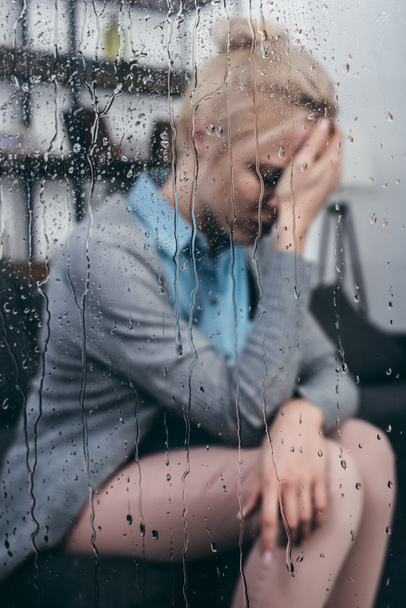 triste mujer adulta tocando la cabeza y teniendo dolor de cabeza en casa a través de la ventana con gotas de lluvia
 - Foto, Imagen
