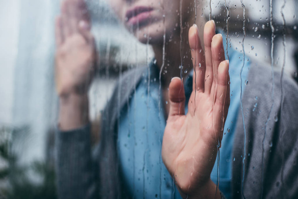 vista recortada de la mujer adulta en casa tocando ventana con gotas de lluvia
 - Foto, imagen
