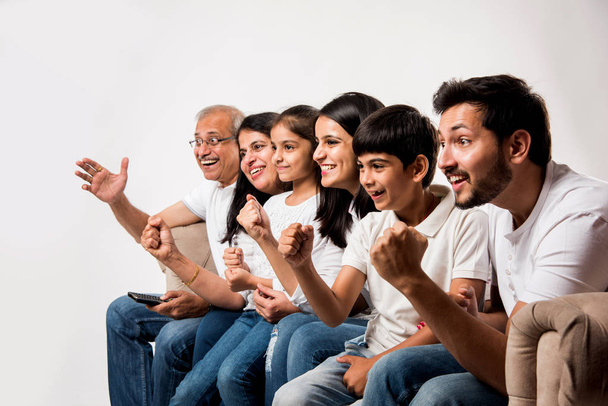 Индийская или азиатская семья, сидя на диване, смотрит телевизор дома - Фото, изображение